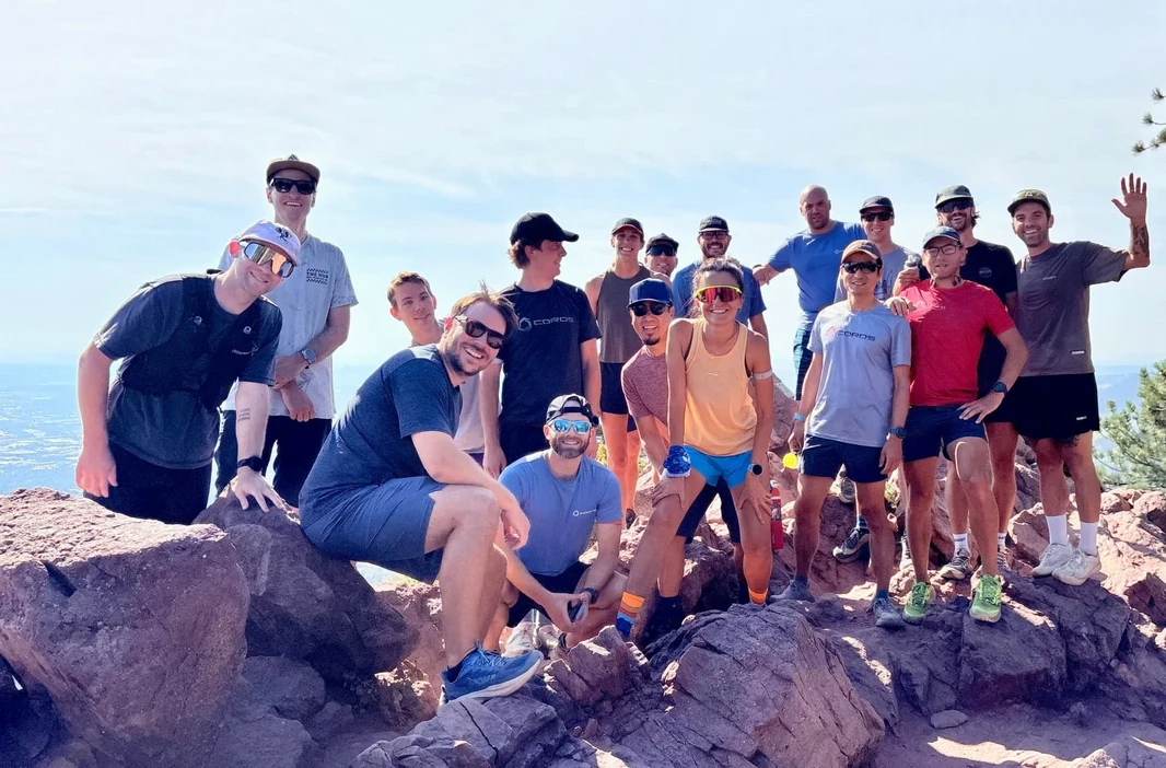 Membri del team COROS posano insieme sulla cima rocciosa di una montagna.