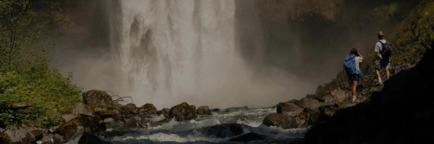 Due escursionisti camminano accanto a una cascata.