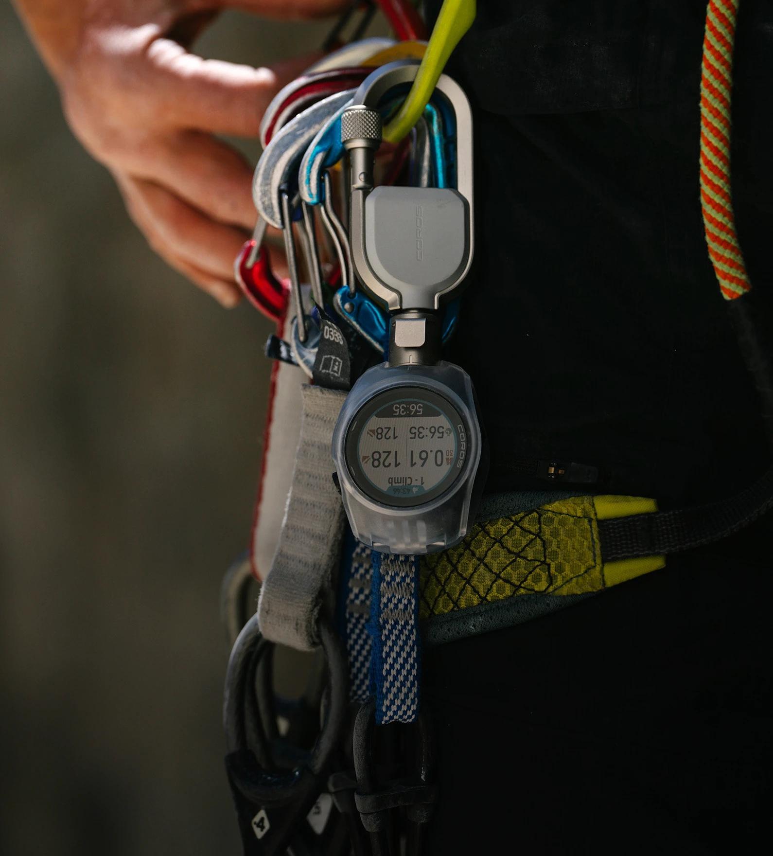 Un mousqueton pour montre COROS APEX 4 solidement fixé à un baudrier à côté de l'équipement d'escalade.