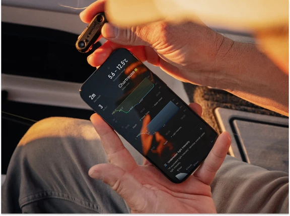 Hands holding the COROS HYDROP sensor and a smartphone displaying underwater data graphs.