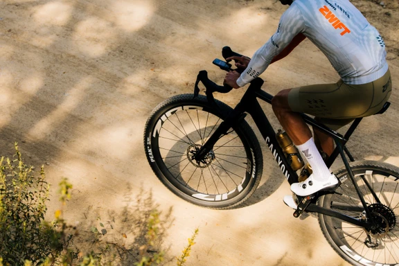 Cyclist on a Canyon bike checks a handlebar device while riding on a dirt path.