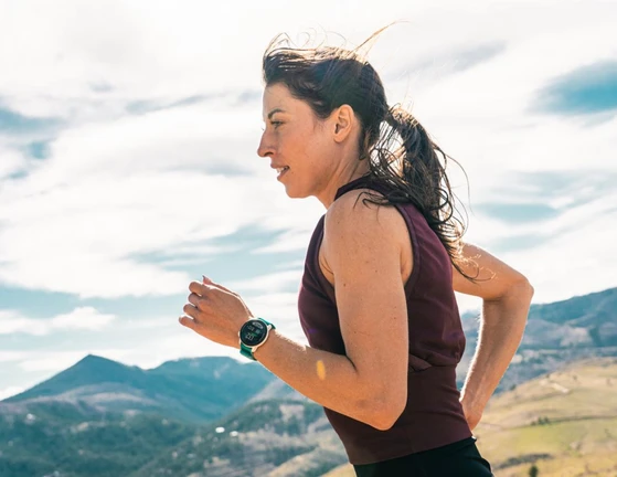 A woman running outdoors with mountains in the background wearing a smartwatch.