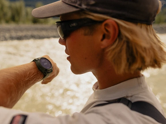 Angler checking a smartwatch on his wrist with a river in the background.