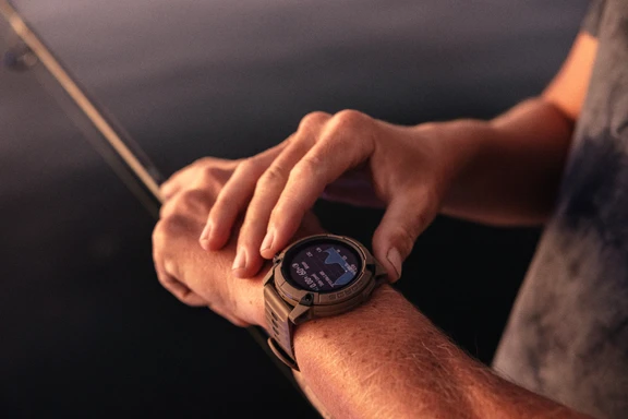 Fisherman checking tide data on a smartwatch while holding a fishing rod.