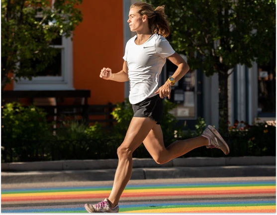 A female runner in a white shirt running on a rainbow crosswalk.