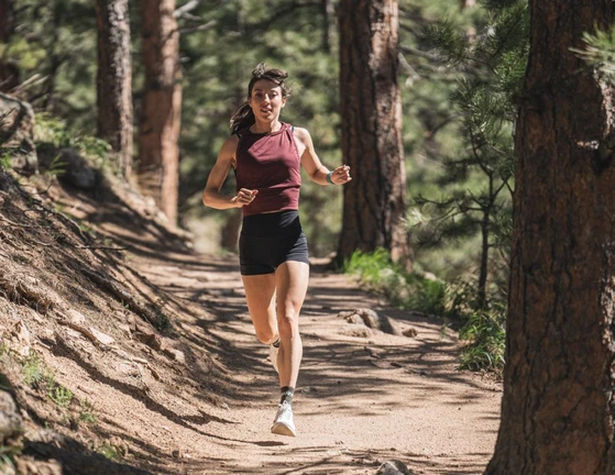 A woman running on a dirt trail through a pine forest.