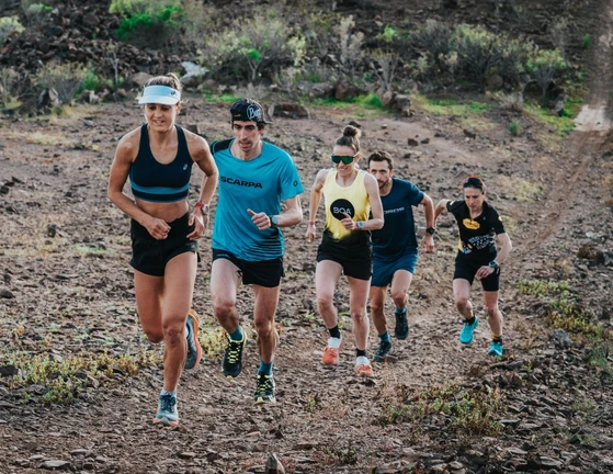 Five runners in athletic gear jogging on a rocky trail.