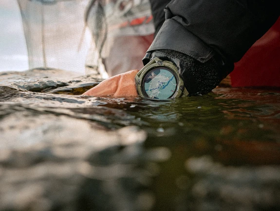 Close-up of a COROS NOMAD watch on a wrist partially submerged in water.