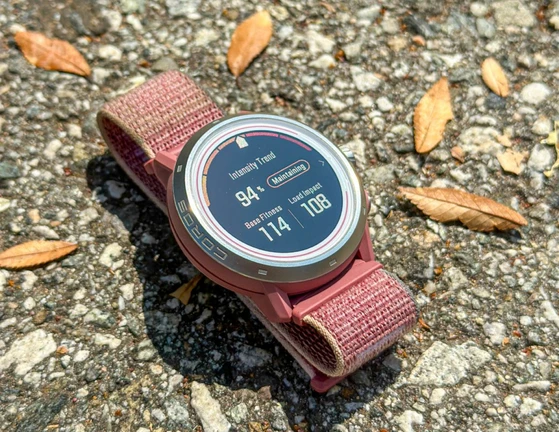 Pink COROS watch on gravel displaying intensity trend, base fitness, and load impact.