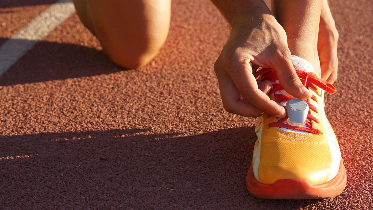 A close-up image of a runner attaching a COROS POD 2 on the left shoe on a track.