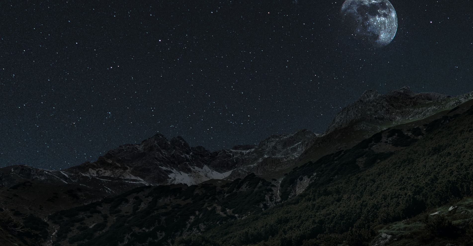 A scenic view of mountains at nighttime with stars in the sky.