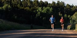 An image of a male and a female runner running on a trail both wearing a COROS PACE 3 watch.