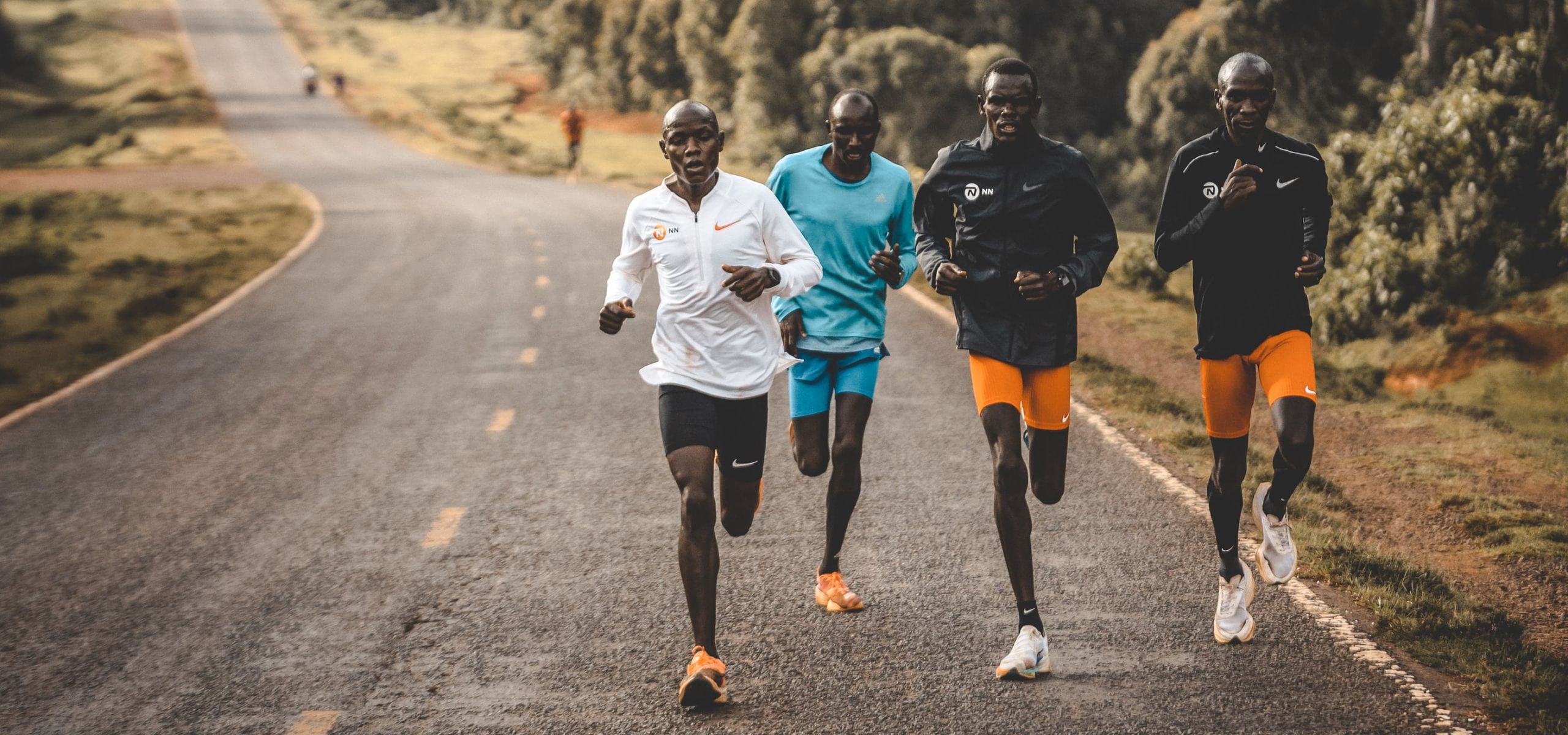 An image of Eliud Kipchoge and three other male runners training on a local road wearing COROS watches.