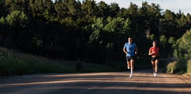 An image of a male and a female runner running on a trail both wearing a COROS PACE 3 watch.